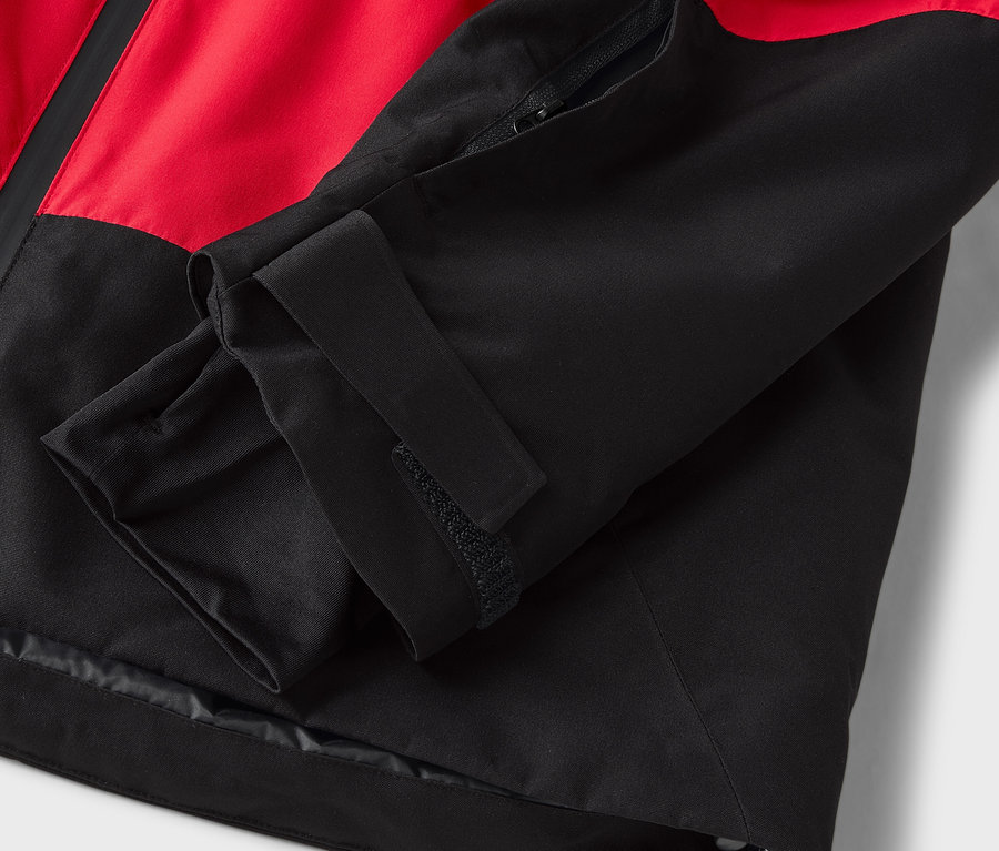 Detailaufnahme einer rot-schwarzen Jacke mit Klettverschluss am Ärmel.