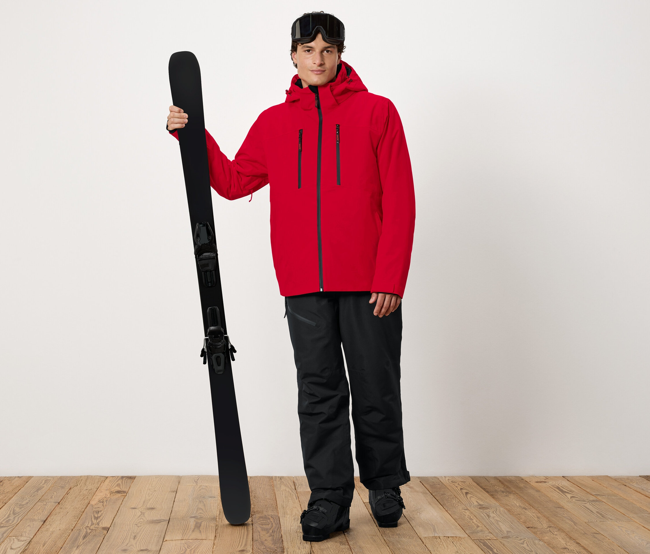 Mann in roter Jacke hält Ski.