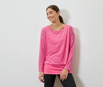 Lächelnde Frau posiert in einem pinkfarbenen Langarmshirt und schwarzen Leggings.