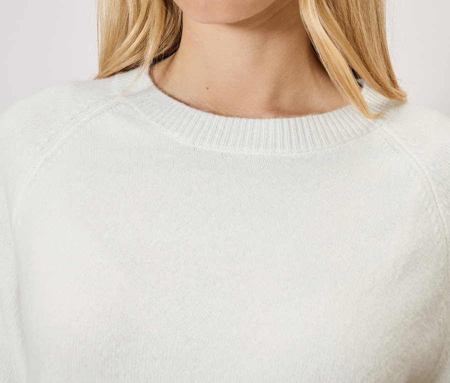 Frau mit blonden Haaren trägt einen weißen Pullover.