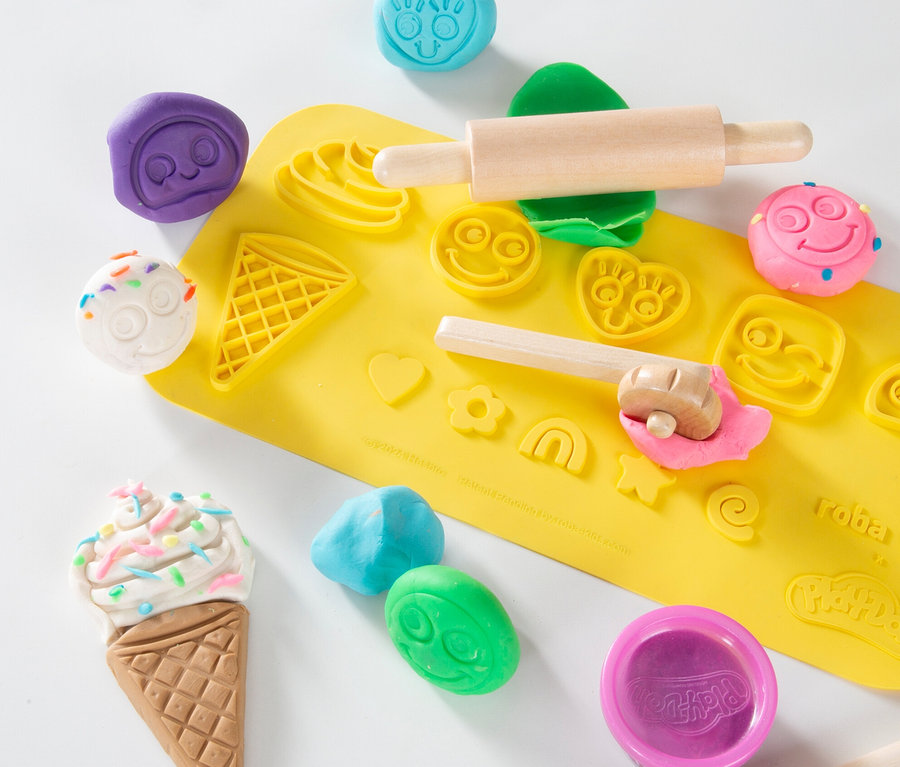 Gelbe Matte mit verschiedenfarbigem Spielteig, einem Holzroller und Modellierwerkzeugen.