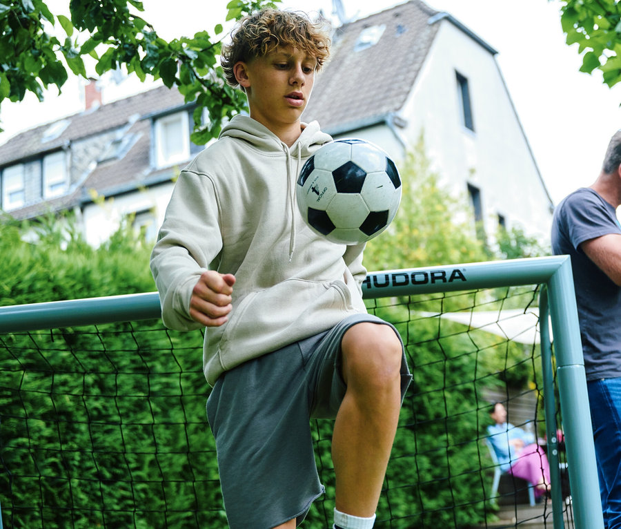 Ein junger Mann jongliert einen Fußball vor einem HUDORA Fußballtor »Expert 180« mit dem Knie.
