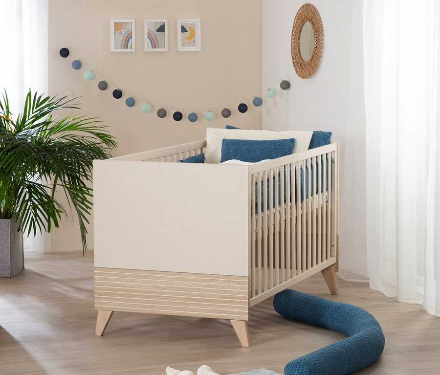 Ein roba Set »Sidney« 3-teilig, Kaschmir Kinderbett mit blauen Kissen und Nestchen steht in einem Zimmer mit einer Pflanze und Dekorationen.