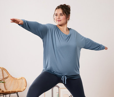 Frau in blauem 2-in-1-Sportshirt und Sporttight macht Yoga auf einer Matte.