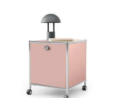 Rosa Rollcontainer mit Chromrahmen und grauer Lampe darauf.