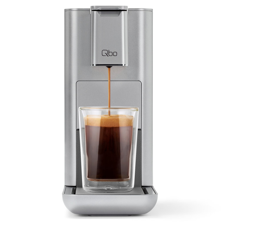 Kaffee läuft aus einer silbernen Qbo Kaffeemaschine in ein Glas.
