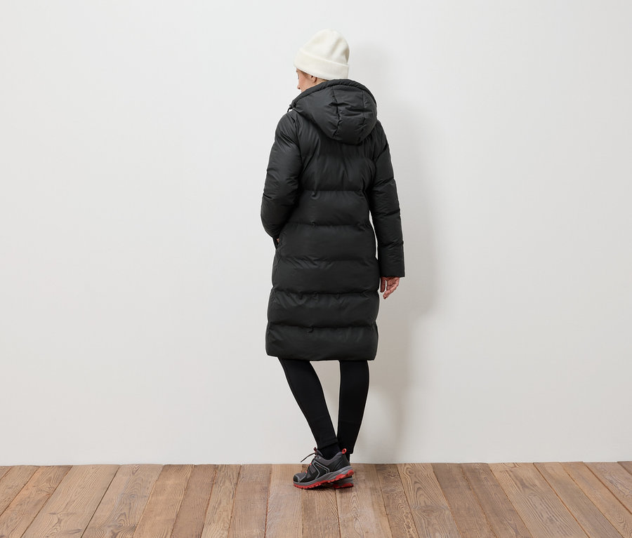 Frau von hinten trägt eine schwarze Daunenjacke, schwarze Leggings und eine weiße Mütze.