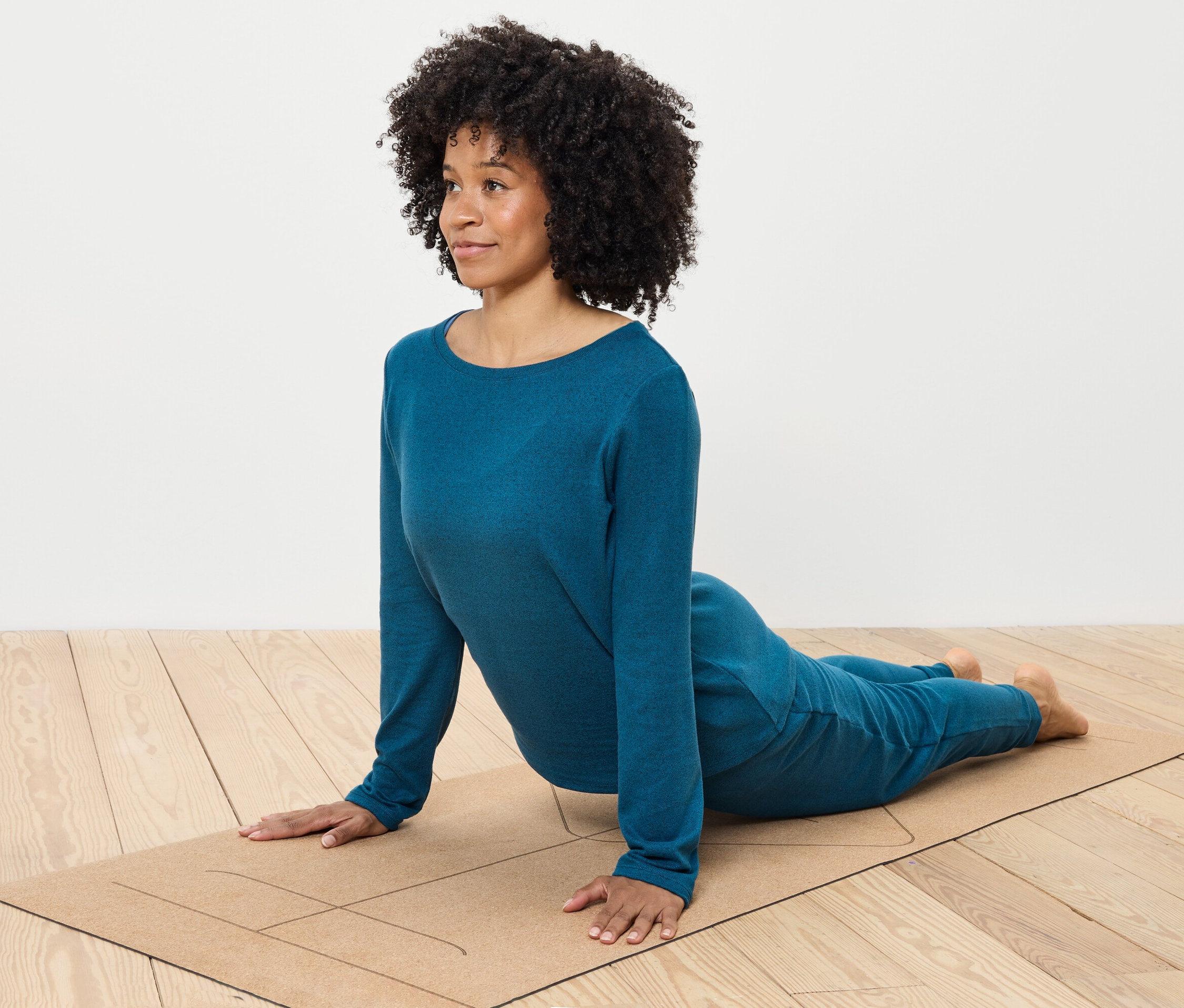 Frau mit lockigem Haar macht Yoga in blauer Kleidung auf einer Matte.