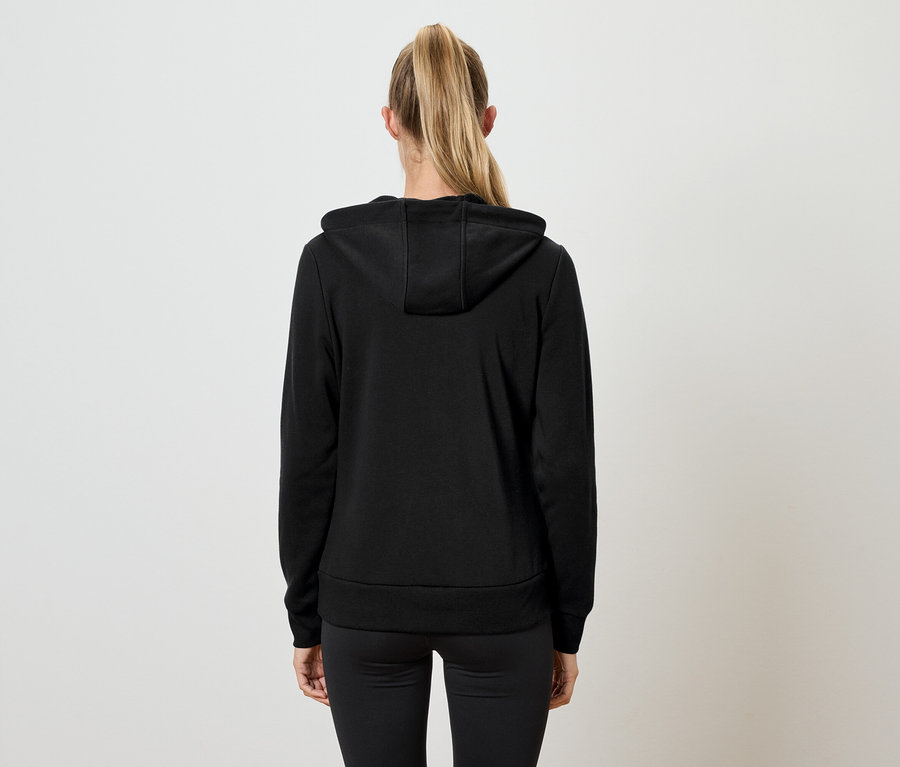 Rückansicht einer Frau mit blonden Haaren, die zu einem Pferdeschwanz zusammengebunden sind. Sie trägt einen schwarzen Kapuzenpullover und eine schwarze Hose.