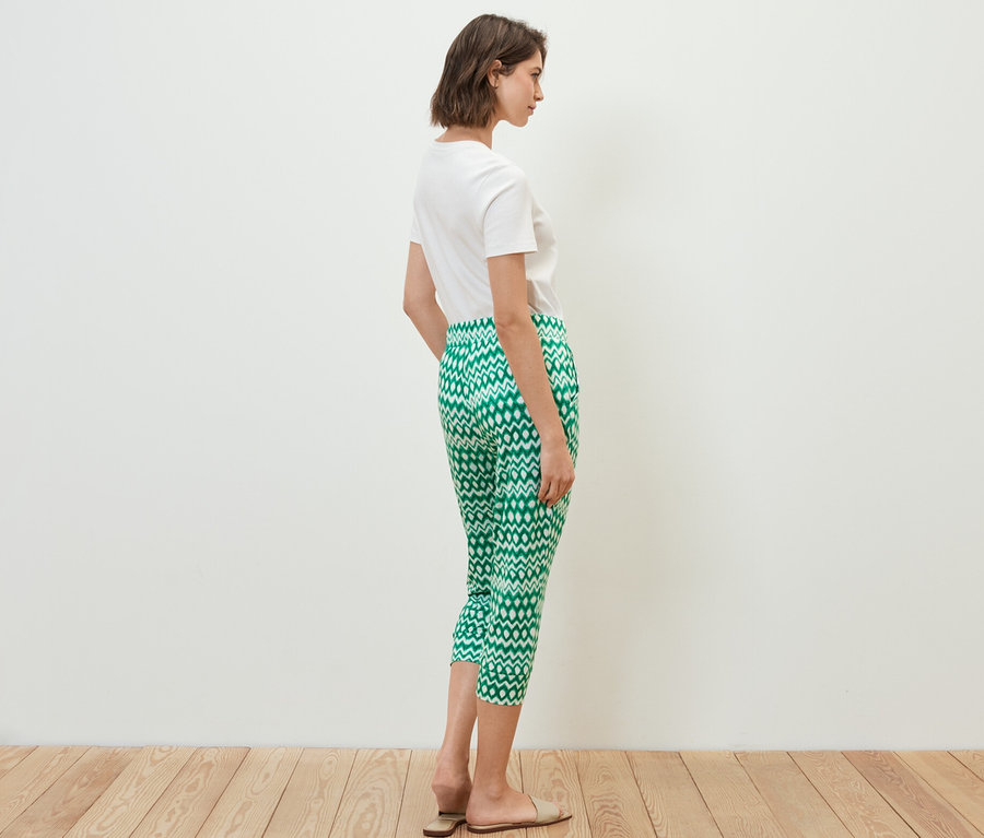 Frau steht seitlich, trägt ein weißes T-Shirt und eine bedruckte 3/4-Jerseyhose.