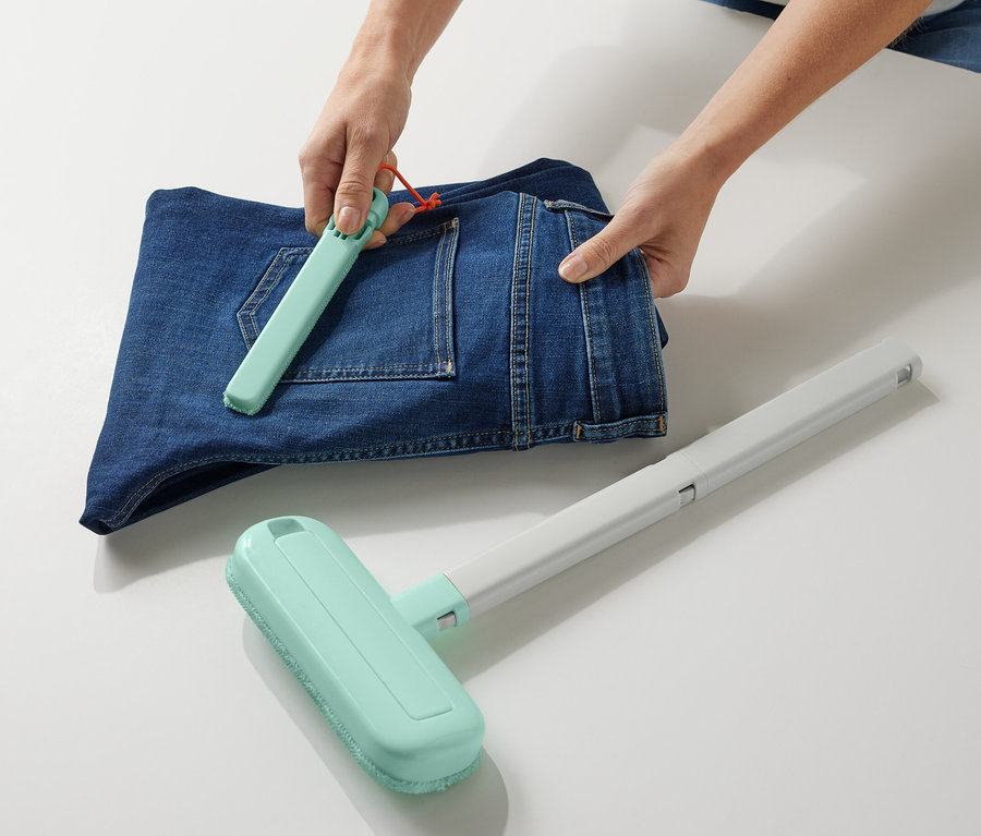 Person verwendet 4-in-1-Textil-Sauberzauber auf gefalteten Jeans.