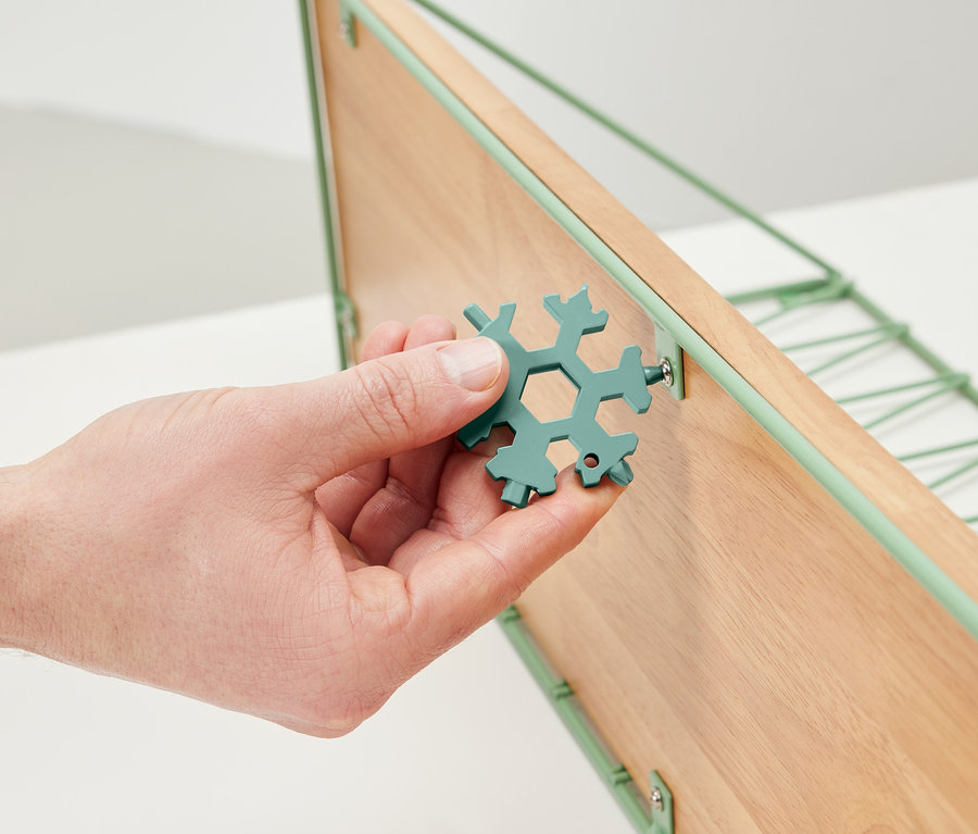 Eine Hand hält einen Multifunktionsschlüssel und zieht eine Schraube an einem Holzregal fest.