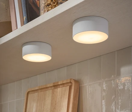 Zwei LED-Multifunktionsleuchten sind an der Unterseite eines Regals befestigt. Auf dem Regal stehen Gläser mit Nüssen und Bücher.