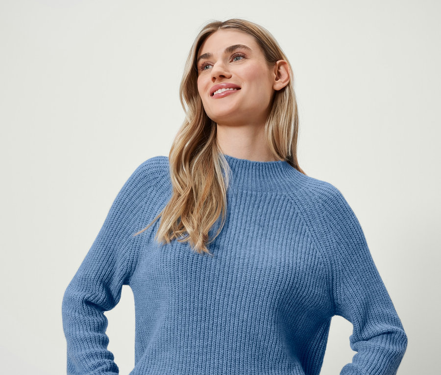 Blonde Frau mit einem Lächeln trägt einen blauen Pullover.
