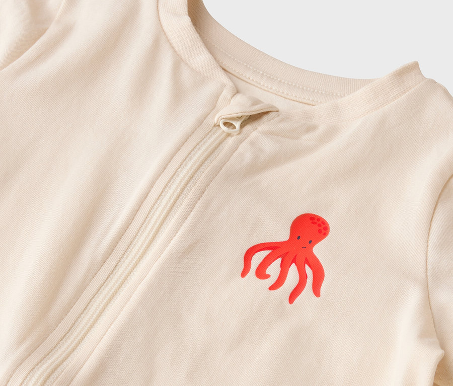 Nahaufnahme eines hellbeigen Baby-Schlafanzugs mit rotem Tintenfisch-Motiv und Reissverschluss.