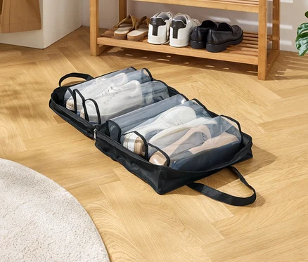 Eine schwarze Schuhtasche mit mehreren Fächern liegt auf einem Holzboden. Die Fächer sind mit verschiedenen Schuhen gefüllt.