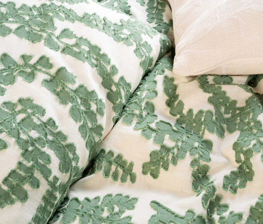 Nahaufnahme von Kissen und Bettwäsche mit grünem Blattmuster und einem cremefarbenen Kissen.