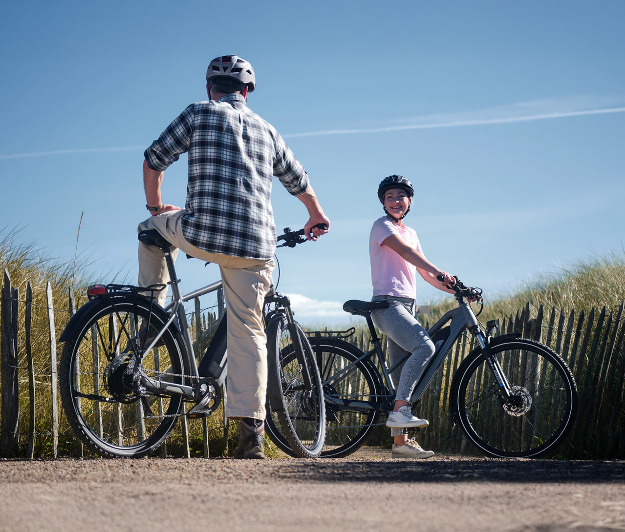 Mann steht mit einem Bein auf einem FISCHER Trekking-E-Bike TERRA 2.2 ACTIVE mit Trapez Rahmen, Frau sitzt lächelnd auf einem ähnlichen Fahrrad.