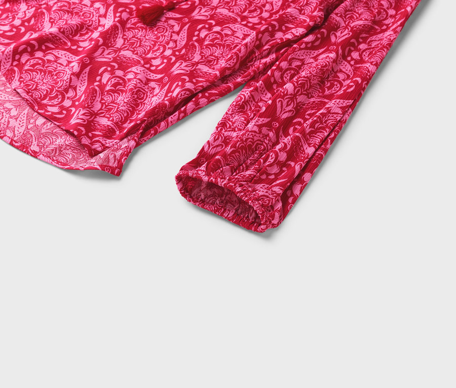 Detailansicht einer roten Bluse mit rosa Blumenmuster und langen Ärmeln.