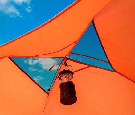 Innenansicht eines orangefarbenen Tambu »HAIKA 2« 2-Personen-Kuppelzelts mit Blick auf einen bewölkten Himmel und einer schwarzen Laterne.