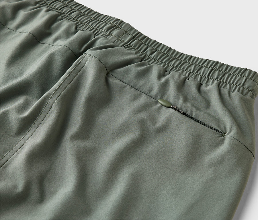 Nahaufnahme einer olivgrünen Hose mit elastischem Bund und Reissverschlusstasche.