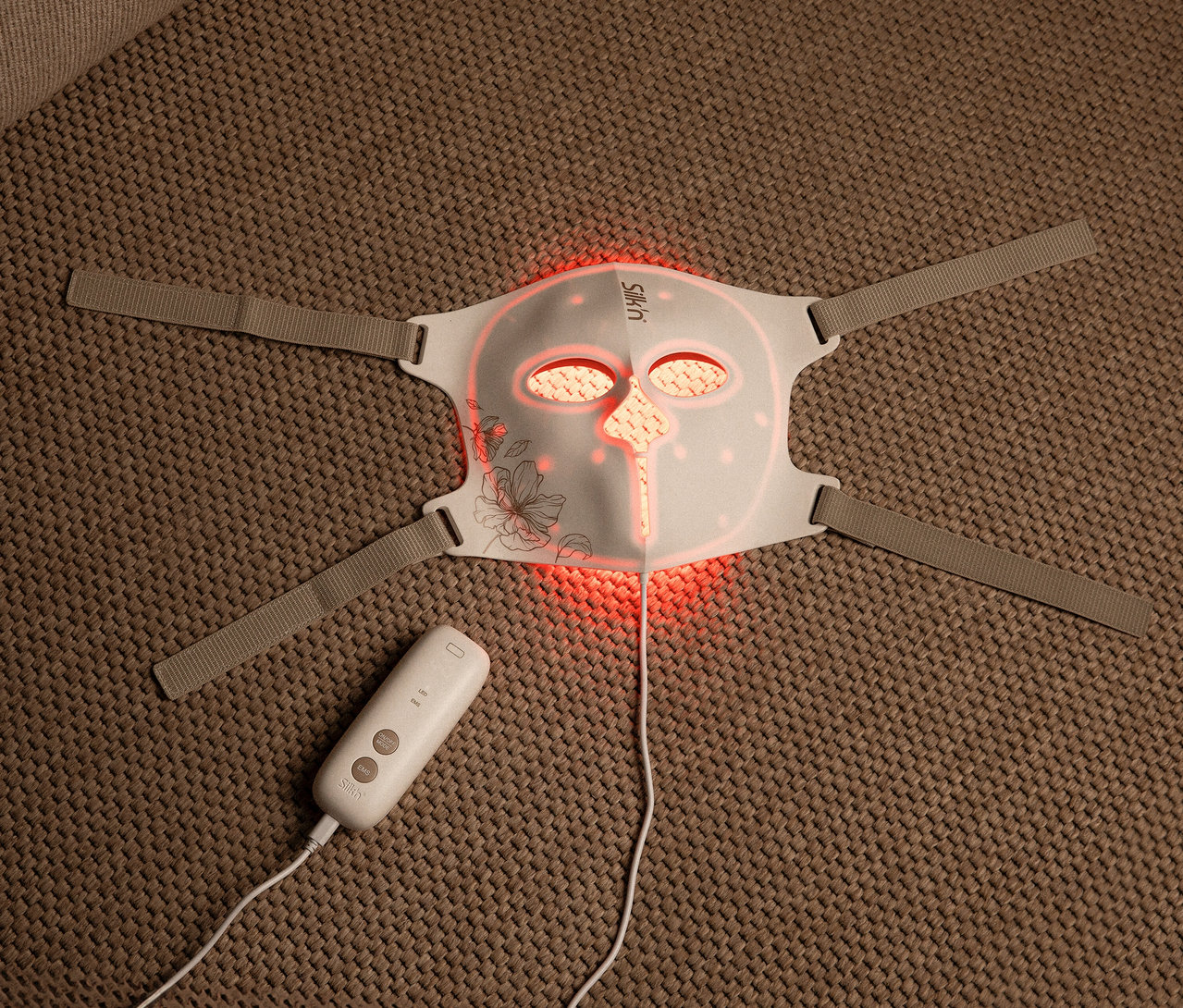 Eine Silk'n LED Gesichtsmaske mit EMS liegt auf einem braunen texturierten Untergrund.