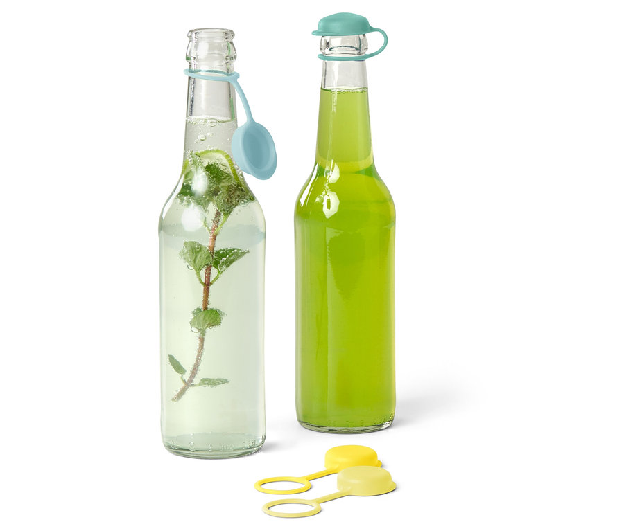 Zwei Glasflaschen, eine mit Minze und Wasser, die andere mit einem grünen Getränk, beide mit farbigen Deckeln.