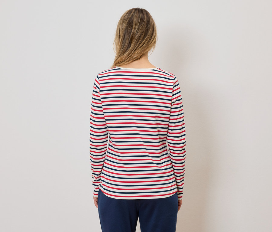 Rückansicht einer Frau mit blonden Haaren, die ein rot-weiß-blau gestreiftes Langarmshirt und eine dunkelblaue Hose trägt.