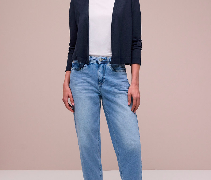 Frau trägt einen dunkelblauen Street One Cardigan über einem weißen T-Shirt, hellblauen Jeans, einem gemusterten Schal und silbernen Sneakers.