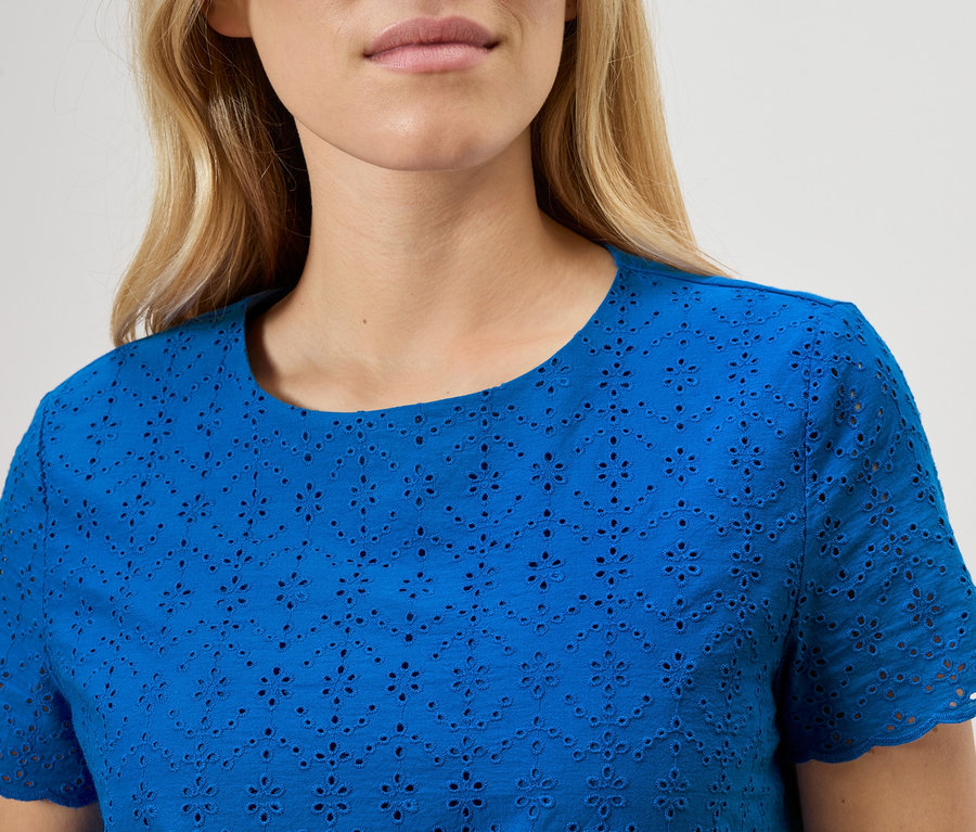 Nahaufnahme einer Frau, die ein blaues Lochstickerei-Oberteil trägt.