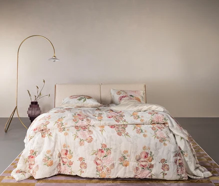 Ein Schlafzimmer mit einem Bett mit floral gemusterter Bettwäsche, einem Nachttisch mit Lampe und einer Vase mit Blumen.