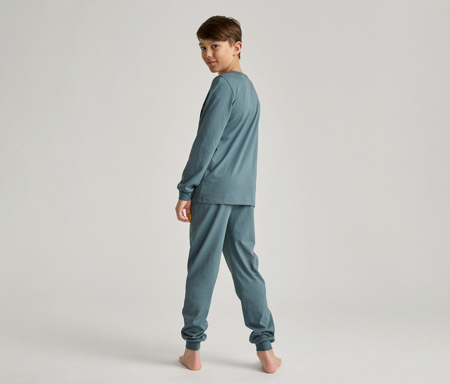 Junge in blaugrünem, langärmligem Pyjama-Set, von hinten gesehen, blickt über die Schulter in die Kamera.