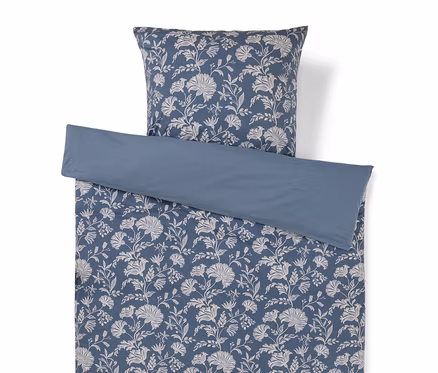 Ein blaues Bettwäscheset mit weißem Blumenmuster und passendem Kissenbezug, mit einem einfarbigen blauen Umschlag oben.