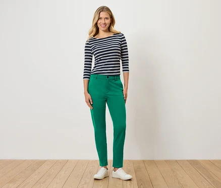 Frau trägt ein blau-weiß gestreiftes Oberteil, eine grüne Hose und weiße Turnschuhe.