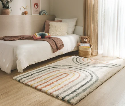 Ein Kinderzimmer mit einem Bett, einem Teppich mit Regenbogenmuster und einem Teddybären in einem Korb.