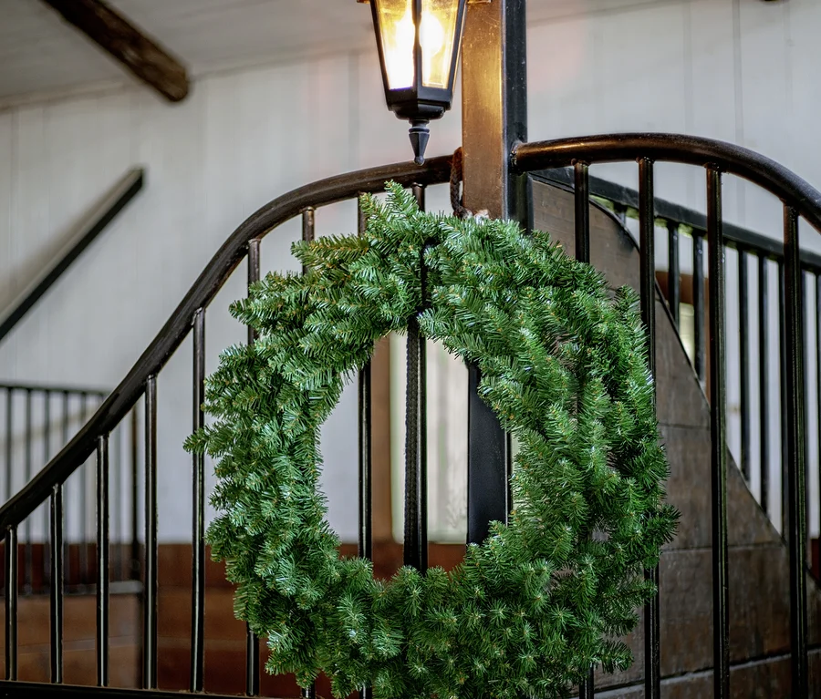 Grüner Weihnachtskranz hängt an einem schwarzen Metalltor, darüber eine leuchtende schwarze Laterne.