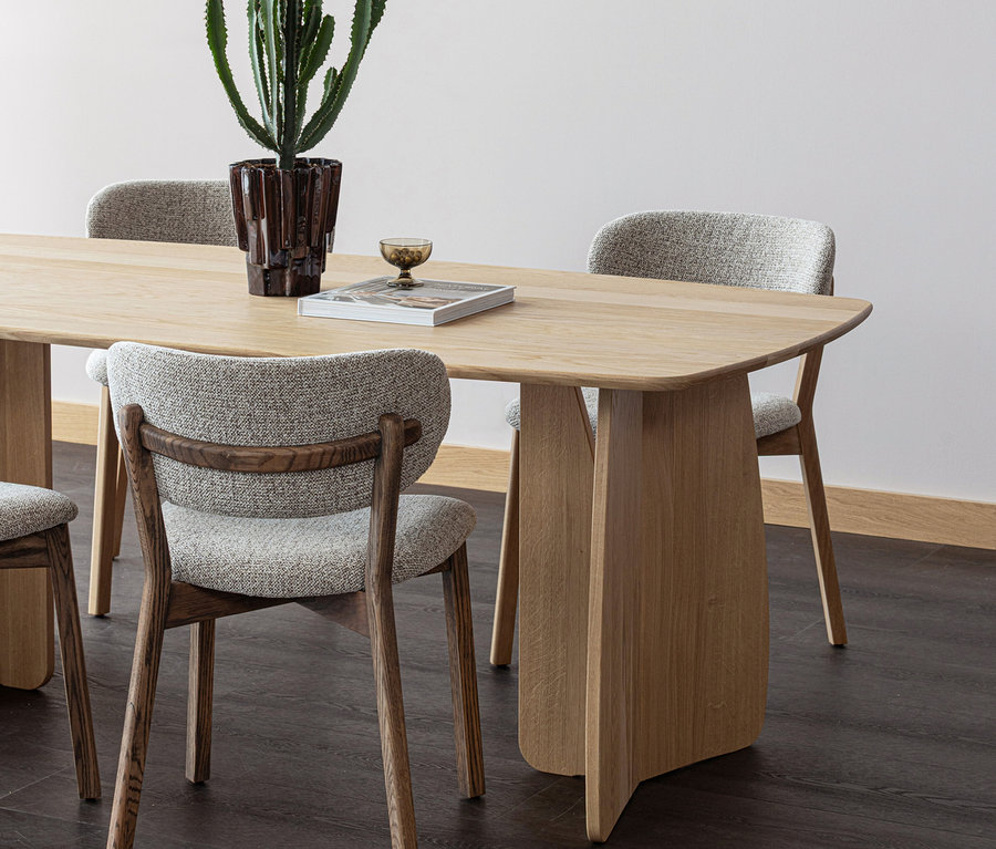 Heller Holztisch mit vier Stühlen mit grauen Polstern und dunklen Holzrahmen. Auf dem Tisch stehen ein Kaktus im Topf, ein Buch und ein kleines Glas.
