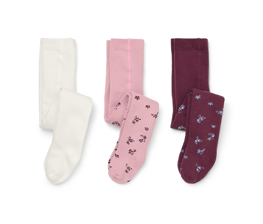 Drei Paar Strumpfhosen auf weißem Hintergrund: eine weiße, eine hellrosa mit floral gemusterten Beinen und eine bordeauxrote mit floral gemusterten Beinen.