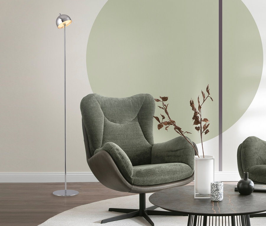 Silberfarbene SCHÖNER WOHNEN-Kollektion Akku-Stehleuchte »Bellis« neben einem grünen Sessel und einem runden Couchtisch mit Dekorationen in einem modern eingerichteten Wohnzimmer.