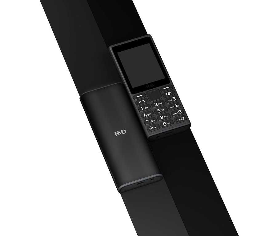 Ein schwarzes HMD 105 4G Mobiltelefon mit Tastenfeld und Display liegt auf einer schwarzen Fläche.