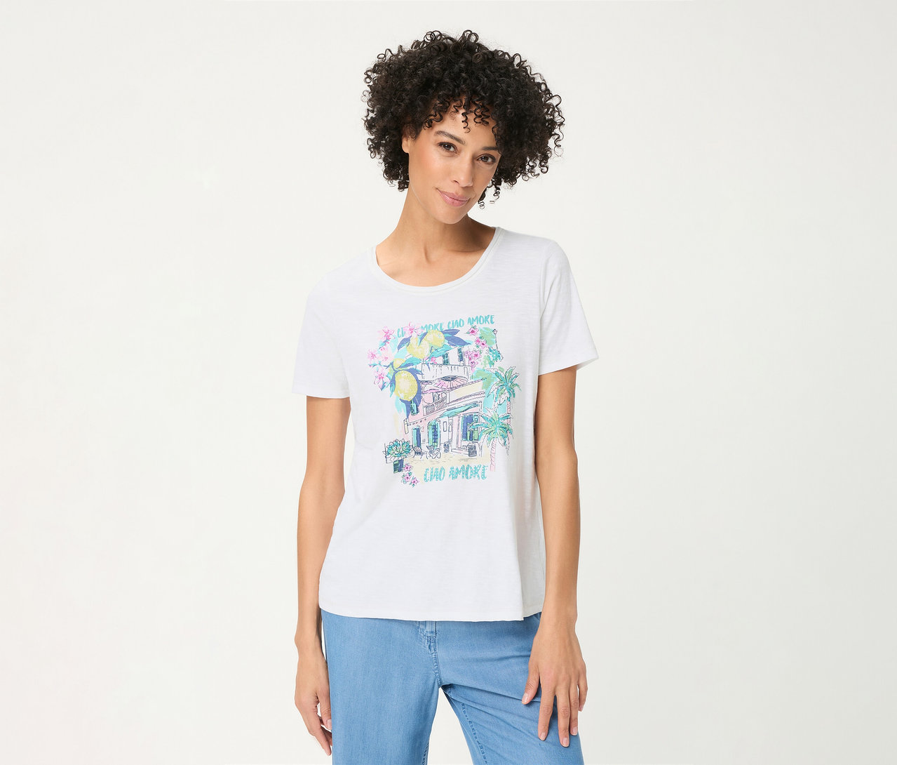 Frau mit lockigem Haar trägt ein weißes Olsen T-Shirt mit einem farbigen Placement-Print aus Zitronen, Blumen, einem Gebäude, Palmen und dem Text "CIAO AMORE", dazu hellblaue Jeans.