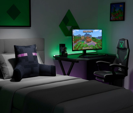 Schlafzimmer mit Gaming-Setup. Ein Bett mit Enderman-Kissen, ein Schreibtisch mit Minecraft-Monitor und ein Gaming-Stuhl mit Creeper-Logo. Grüne und violette Beleuchtung.