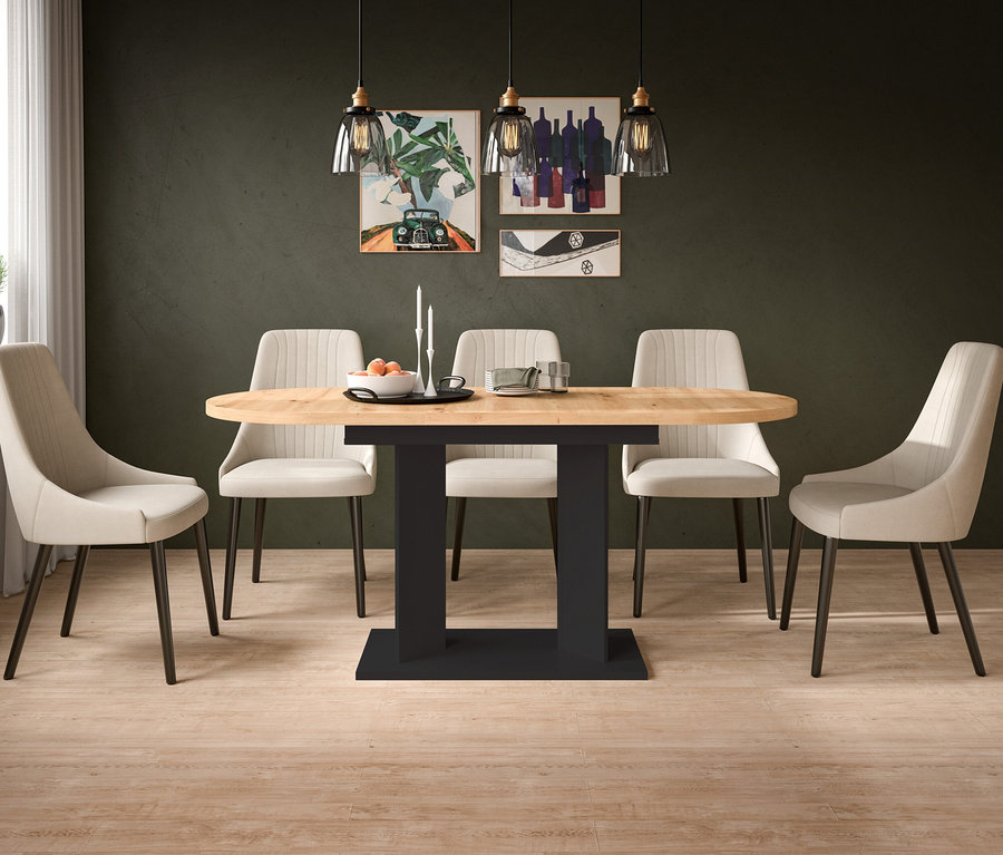 Ein Esszimmer mit einem ovalen hellen Holztisch auf einem schwarzen Säulenfuß, umgeben von sechs beigen Polsterstühlen. Die dunkelgrüne Wand im Hintergrund ist mit drei gerahmten Kunstwerken und drei Pendelleuchten dekoriert. Auf dem Tisch stehen eine Schale mit Orangen, Kerzenständer und Tassen. Heller Holzfußboden und ein Fenster mit weißen Vorhängen sind sichtbar.
