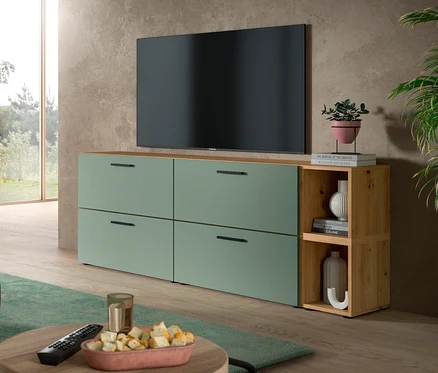 Ein Wohnzimmer mit einem großen schwarzen Fernseher über einer grünen xonox Wohnkombination »The One«. Die Kombination hat vier grüne Schubladen und ein offenes Holzregal mit Dekoartikeln. Ein Couchtisch mit Snacks und Fernbedienung steht im Vordergrund.