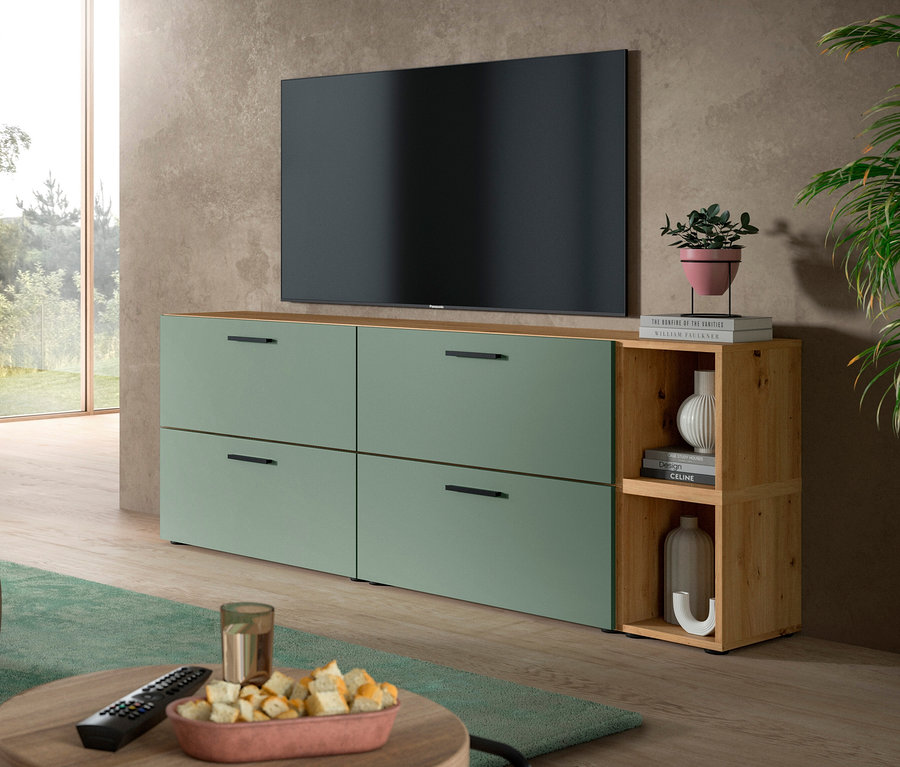 Ein Wohnzimmer mit einem großen schwarzen Fernseher über einer grünen xonox Wohnkombination »The One«. Die Kombination hat vier grüne Schubladen und ein offenes Holzregal mit Dekoartikeln. Ein Couchtisch mit Snacks und Fernbedienung steht im Vordergrund.