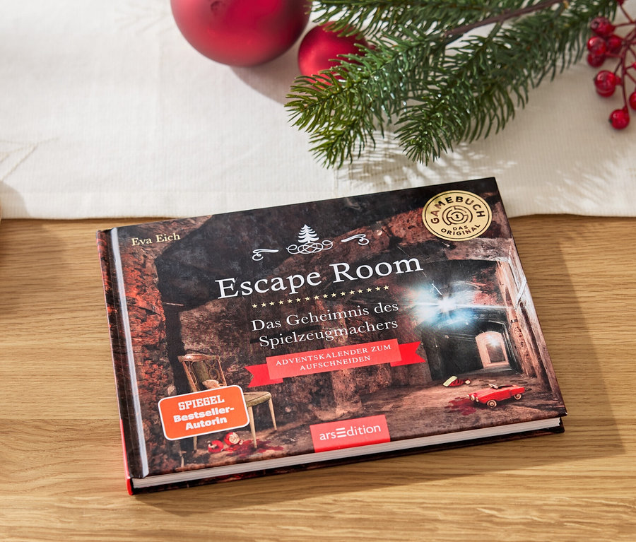 Ein Escape Room Buch liegt auf einem Holztisch neben einem Teller mit Lebkuchen und Weihnachtsdekoration.