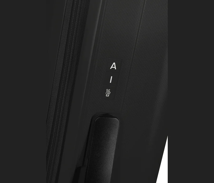 Nahaufnahme eines schwarzen American Tourister Rejoy Spinner Koffers mit Reißverschluss, einem Etikett mit 'A', 'I' und einem Friedenszeichen sowie einem schwarzen Griff.