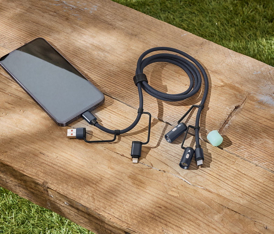 Ein graues Smartphone ist mit einem schwarzen, geflochtenen Multi-Ladekabel auf einer Holzbank verbunden.