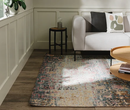 Wohnzimmerecke mit hellgrauem Sofa, Holztisch und einem Benuta Teppich »Frencie« auf Holzfußboden. Der Teppich zeigt ein abstraktes Muster in Rosa, Blau, Gelb und Beige.
