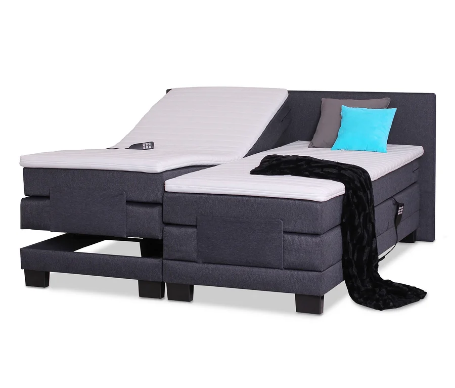 Detailansicht eines motorisch verstellbaren Bettes. Eine Seite ist hochgefahren, auf dem Bett liegen eine Fernbedienung, ein graues und ein türkisfarbenes Kissen sowie eine schwarze Decke. sun garden Boxspringbett mit motorischer Verstellung, 180 x 200 cm